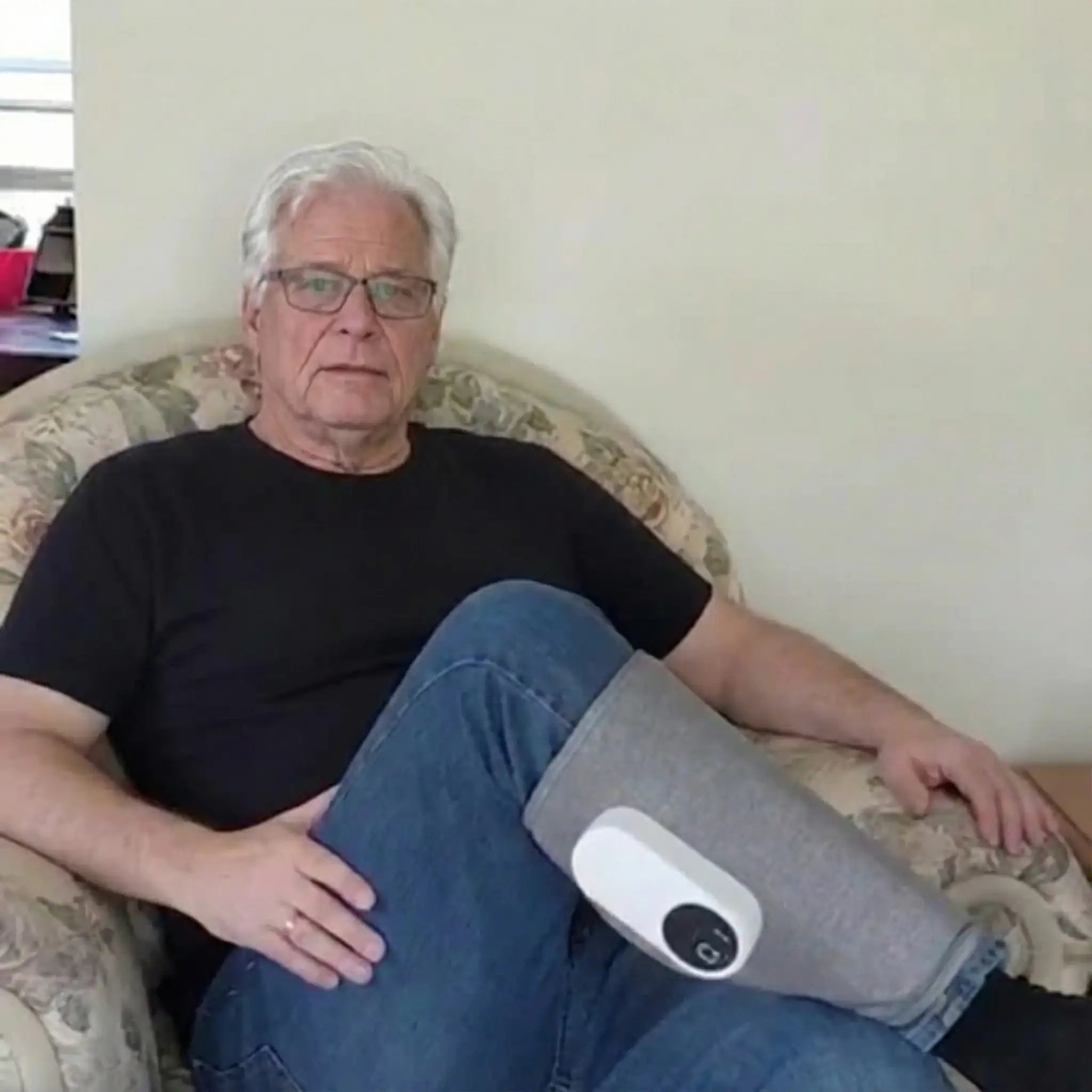 Older man relaxing in armchair using the Recovie leg massager on his calf
